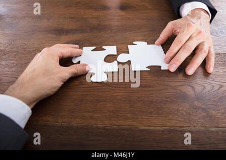 Angolo di Alta Vista di due imprenditori il collegamento di pezzi di un puzzle sulla scrivania in legno Foto Stock