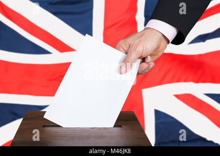 Imprenditore mettendo mano votare nelle urne nella parte anteriore del Regno Unito Bandiera Foto Stock