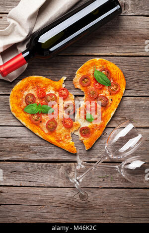 A forma di cuore la pizza con pomodoro e mozzarella e vino rosso bottiglia. Il giorno di San Valentino biglietto di auguri. Vista superiore Foto Stock