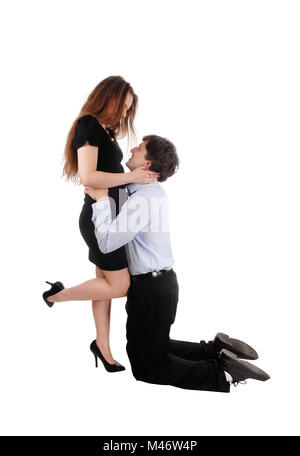 Una giovane coppia amarsi, egli è in ginocchio per lei e abbracciando il suo, guardando ogni altro, isolato per sfondo bianco Foto Stock