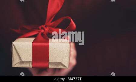 Femmina mani teen apre imbarcazioni carta regalo con fiocco rosso Foto Stock