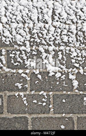 Parte di una parete di mattoni parzialmente coperto da neve fresca Foto Stock