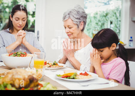 Madre e figlia con la nonna pregando al tavolo da pranzo Foto Stock