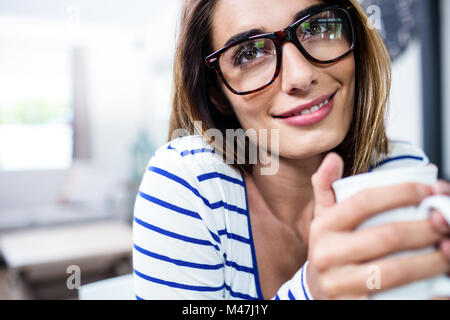 Contemplato il giovane donna sorridente mentre si tiene il caffè Foto Stock