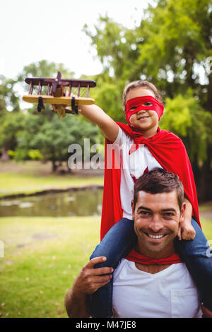 Ragazza in costume da supereroe seduti sulle spalle dei padri Foto Stock