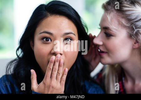 Giovane donna whispering a sorpresa amico femmina Foto Stock