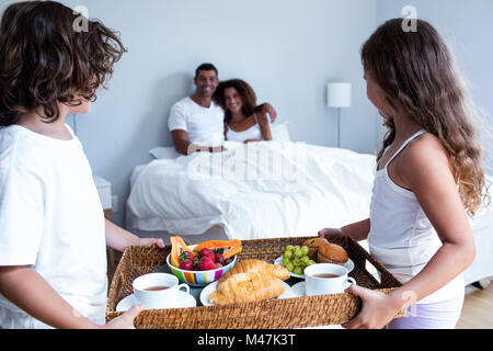 La figlia e il figlio che porta il vassoio colazione per i genitori Foto Stock