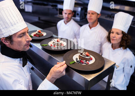 Capo chef ispezione piatti da dessert su alla stazione di ordine Foto Stock