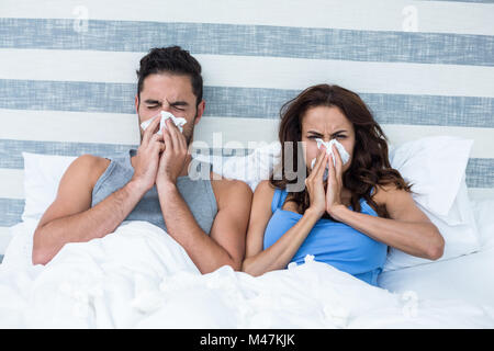 Coppia giovane che copre il naso mentre starnuti sul letto Foto Stock