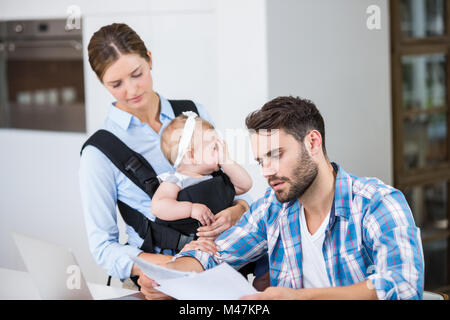 L'uomo la lettura dei documenti mentre la moglie Trasporto bambini Foto Stock