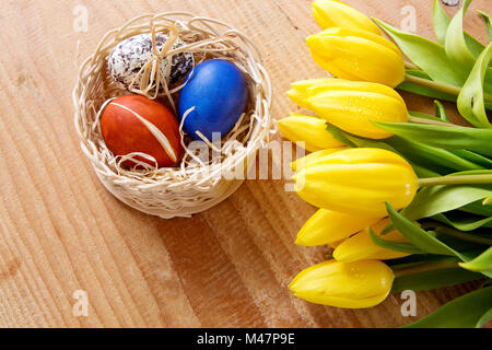 Cesto di pasqua con uova colorate e tulipani gialli. Foto Stock