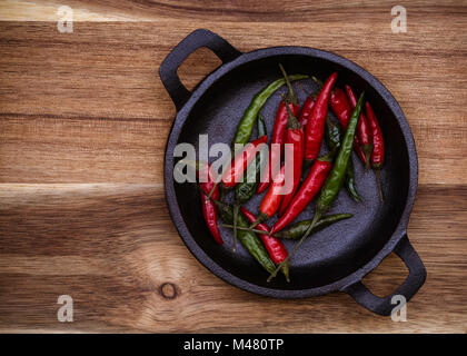 Rosso e peperoncini verdi in una ghisa nera ciotola su un sfondo di legno con spazio di copia Foto Stock