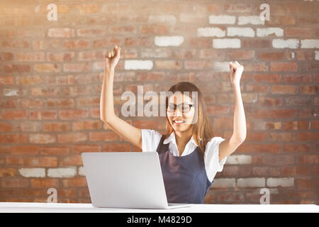 Immagine composita di felice imprenditrice utilizzando laptop e bracci di sollevamento Foto Stock