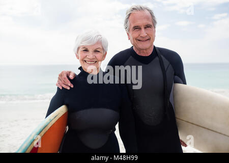 Coppia senior in wetsuit tenendo la tavola da surf in spiaggia Foto Stock