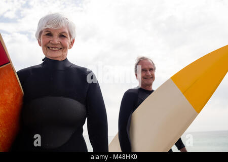 Coppia senior in wetsuit tenendo la tavola da surf in spiaggia Foto Stock