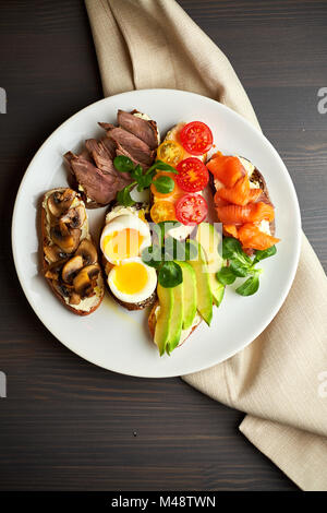 La bruschetta, assortiti, diversi ripieni, su piastre con un soft-uovo sodo in medio Foto Stock