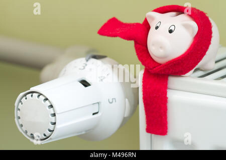 Risparmiare denaro concetto di riscaldamento con termostato e salvadanaio su sfondo verde Foto Stock