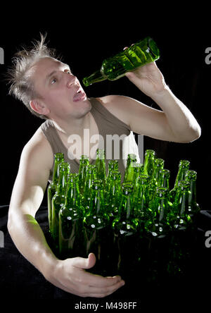 L'ubriaco uomo si siede con un mucchio di bottiglie di birra Foto Stock