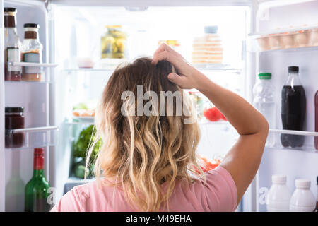 Vista posteriore di un confuso donna cercando in frigorifero aperto a casa Foto Stock