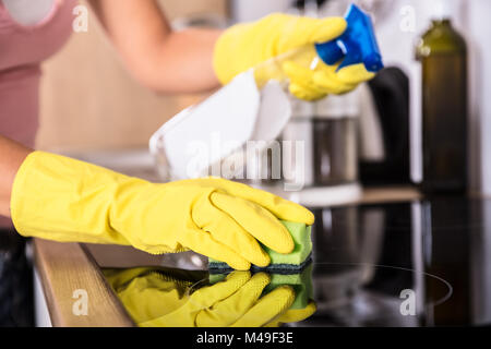 Close-up di persona pulizia delle mani Fornello ad induzione in cucina con la bottiglia spray e spugna Foto Stock
