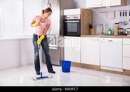 Sorridente Giovane Donna di pulizia Piano Cottura Con Mop in cucina a casa Foto Stock