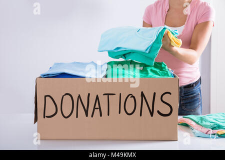 Close-up di una donna di mettere i vestiti all'interno di casella di donazione Foto Stock