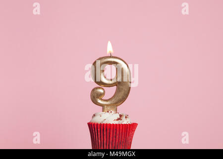 Numero 9 gold candela in una tortina contro un pastello sfondo rosa Foto Stock