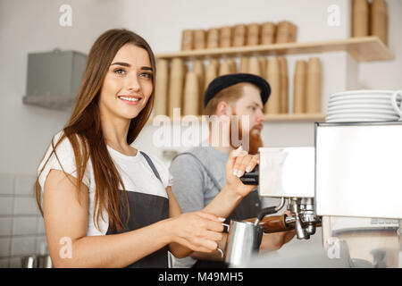 Caffè il concetto di Business - Ritratto di signora barista grembiule in preparazione per la cottura a vapore e il latte per il caffè ordine con il suo partner in piedi presso il cafe. Foto Stock