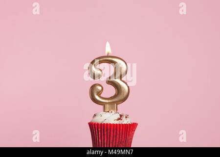 Numero 3 gold candela in una tortina contro un pastello sfondo rosa Foto Stock
