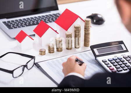 Commercianti calcolo delle imposte nella parte anteriore dei modelli della casa e delle monete impilate con occhiali e calcolatrice Foto Stock
