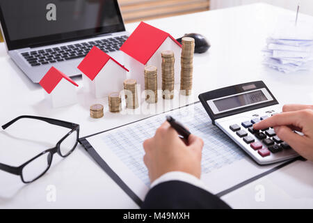 Commercianti calcolo delle imposte nella parte anteriore dei modelli della casa e delle monete impilate con occhiali e calcolatrice Foto Stock
