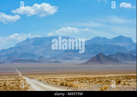 La strada attraverso il deserto pietroso di andare a una distanza, all'orizzonte maestose creste tower Foto Stock