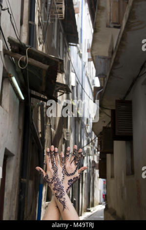 Donna di henna decorate mani giunte in posizione verticale in un vicolo in Stone Town, Zanzibar, Tanzania in una luminosa e soleggiata giornata Foto Stock