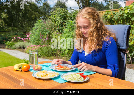 Giovane donna caucasica di consumare la colazione in giardino Foto Stock