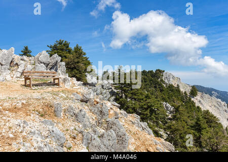 Panca sulla montagna rocciosa con alberi e cielo blu Foto Stock