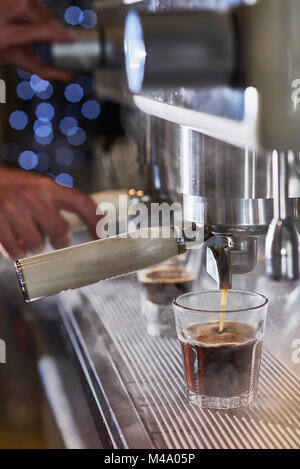 Barista rendendo un caffè espresso con un classico italiano macchina caffè con vapore in background. Foto Stock