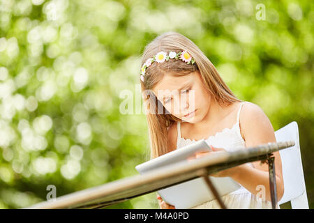 Bambina sembra curioso e focalizzata sul suo computer tablet in giardino Foto Stock