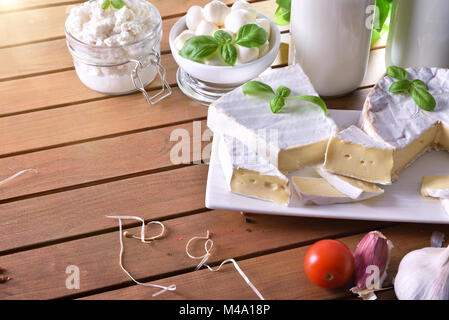 Assortimento di caseificio artigianale prodotti su di un tavolo di legno in cucina rustica. Vista in elevazione. Composizione orizzontale Foto Stock