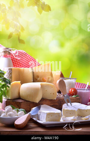Grande assortimento di caseificio artigianale prodotti su di un tavolo di legno con sfondo verde con foglie. Vista in elevazione. Composizione verticale Foto Stock