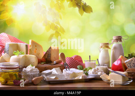 Grande assortimento di caseificio artigianale prodotti su di un tavolo di legno con sfondo verde con foglie. Vista frontale. Composizione orizzontale Foto Stock