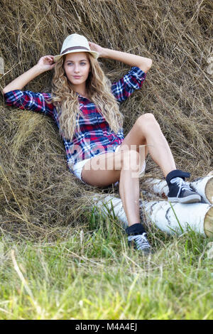 Giovane biondo country girl in hat vicino haystacks Foto Stock