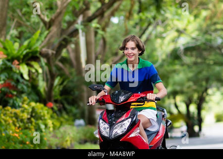 Adolescente scooter di equitazione. Ragazzo adolescente divertimento sul giro in moto sul suo modo di scuola. Studente su motociclo in città tropicale. Viaggi e trasporti per Foto Stock