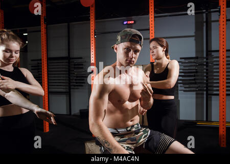 Gruppo di tre felice muscolare di femmine e maschi adulti seduti insieme sulla scatola come buoni amici in palestra con diffusore di grandi dimensioni in background dopo un difficile Foto Stock