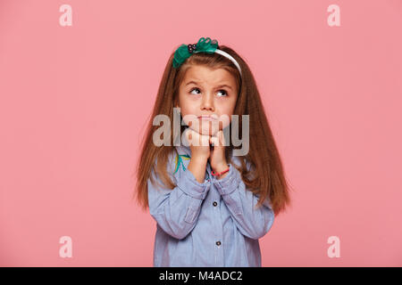 Close up foto di adorabili schoolgirl 5-6 anni appoggiando la sua testa con i pugni, essendo sconvolto o sognare isolate su sfondo rosa Foto Stock