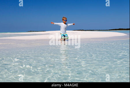 Un ragazzo viene eseguito su in acqua su una piccola barra di sabbia isola nelle limpide acque vicino all uomo-O-War Cay appena fuori dell'isola di Grande Exuma nelle Bahamas. Foto Stock