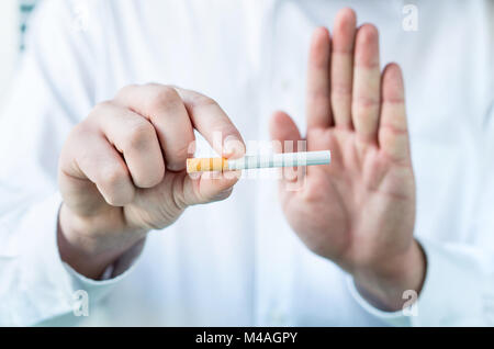 Medico dice di smettere di fumare. Azienda sigaretta tra le dita e che mostra un segno di stop con la mano. Foto Stock