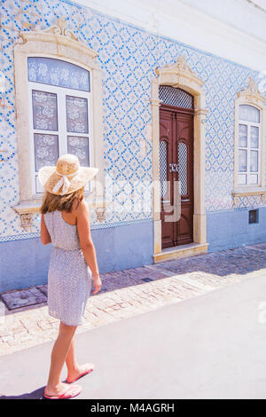 Donna che indossa un cappello, camminando per le strade di Albufeira. Piastrelle tradizionali - azulejos coperti di casa sulla strada. Algarve Portogallo Foto Stock