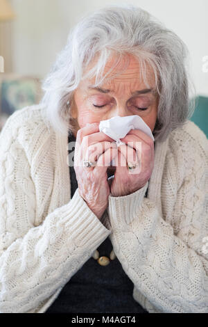 Senior donna con Flu soffia il naso a casa Foto Stock