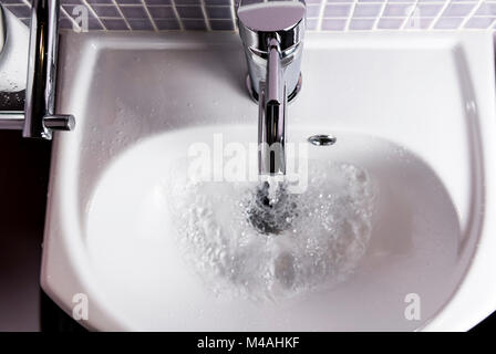 Acqua che scorre da un bagno rubinetto, in un lavandino. Foto Stock