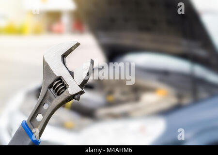 Riparazione auto, manutenzione e ispezione del veicolo concetto. Chiave e con una vettura al di sotto del cofano motore e vista. Messa a fuoco selettiva per strumento di fissaggio. Foto Stock